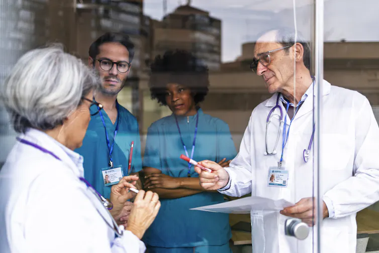 four medical workers in white coats and scrubs in discussion