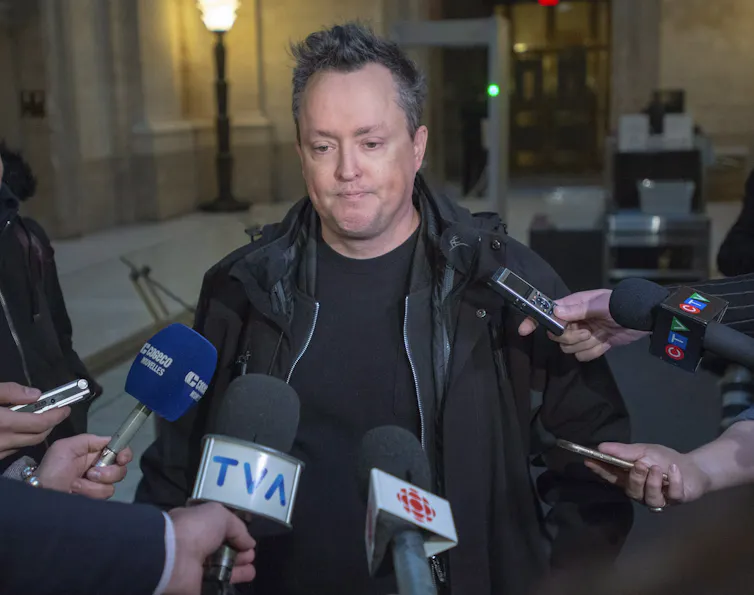 A man is standing in front of press with their hand holding microphones.