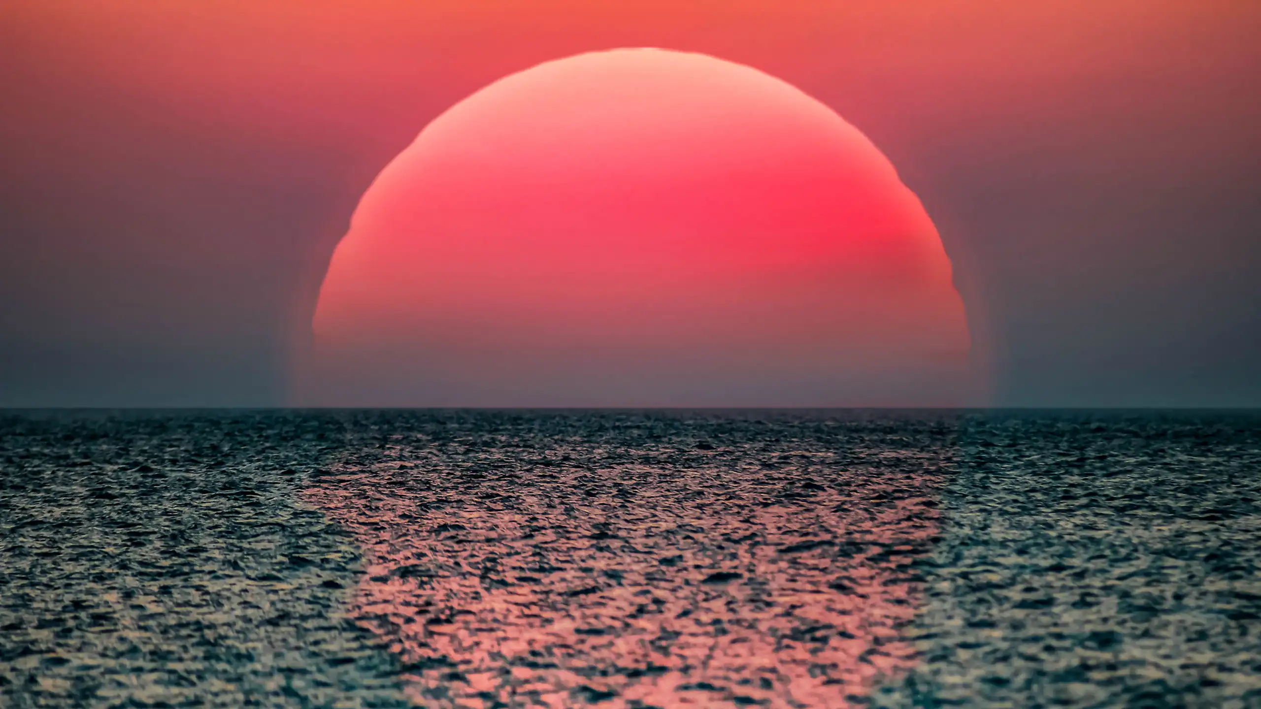 large red sun setting over grey ocean.