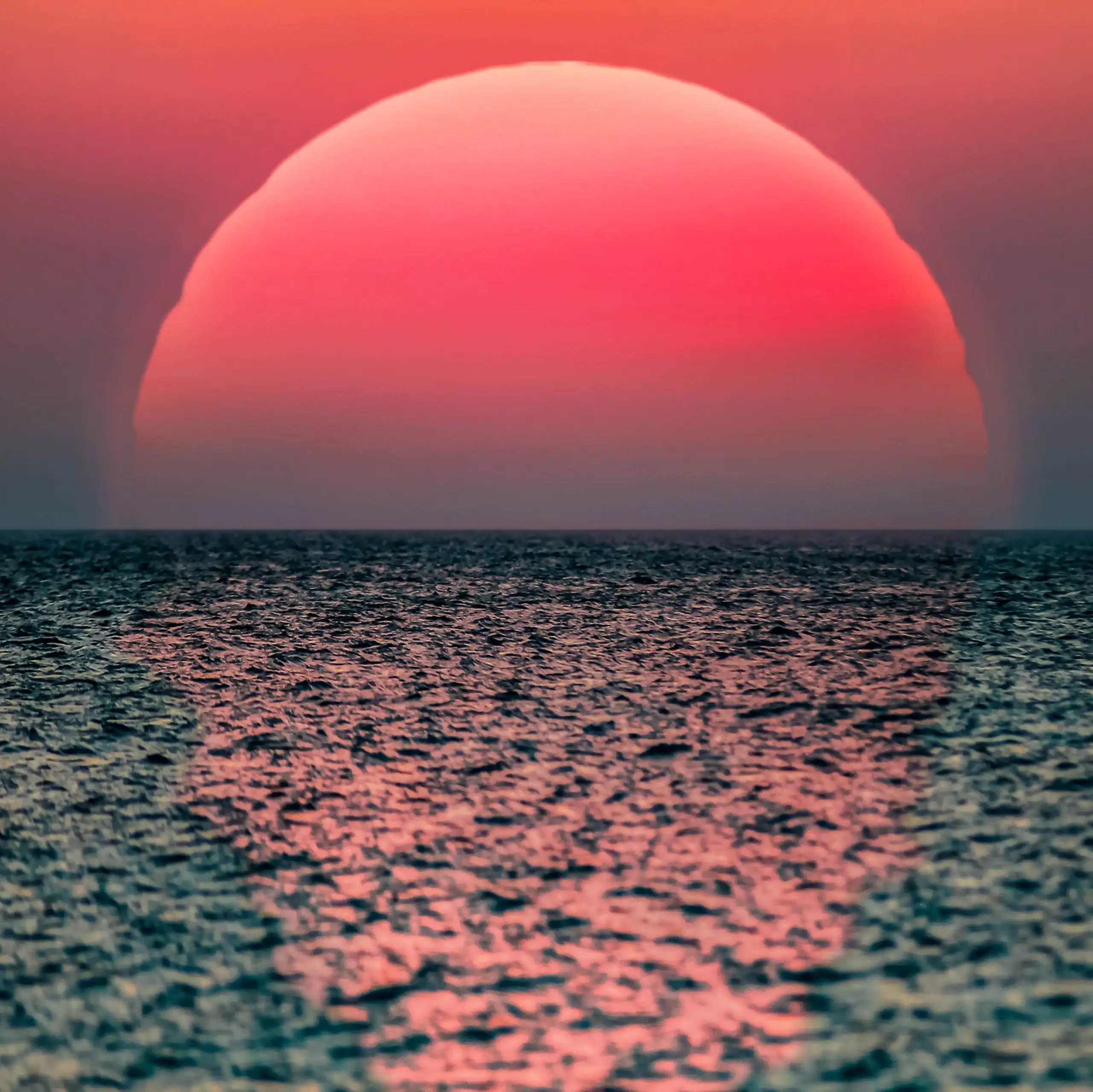 large red sun setting over grey ocean.