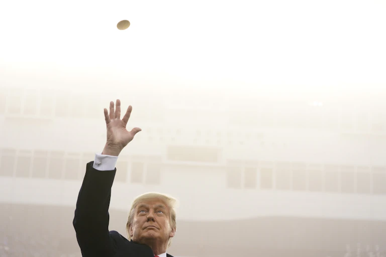 A man in a suit tossing a gold coin in the air.