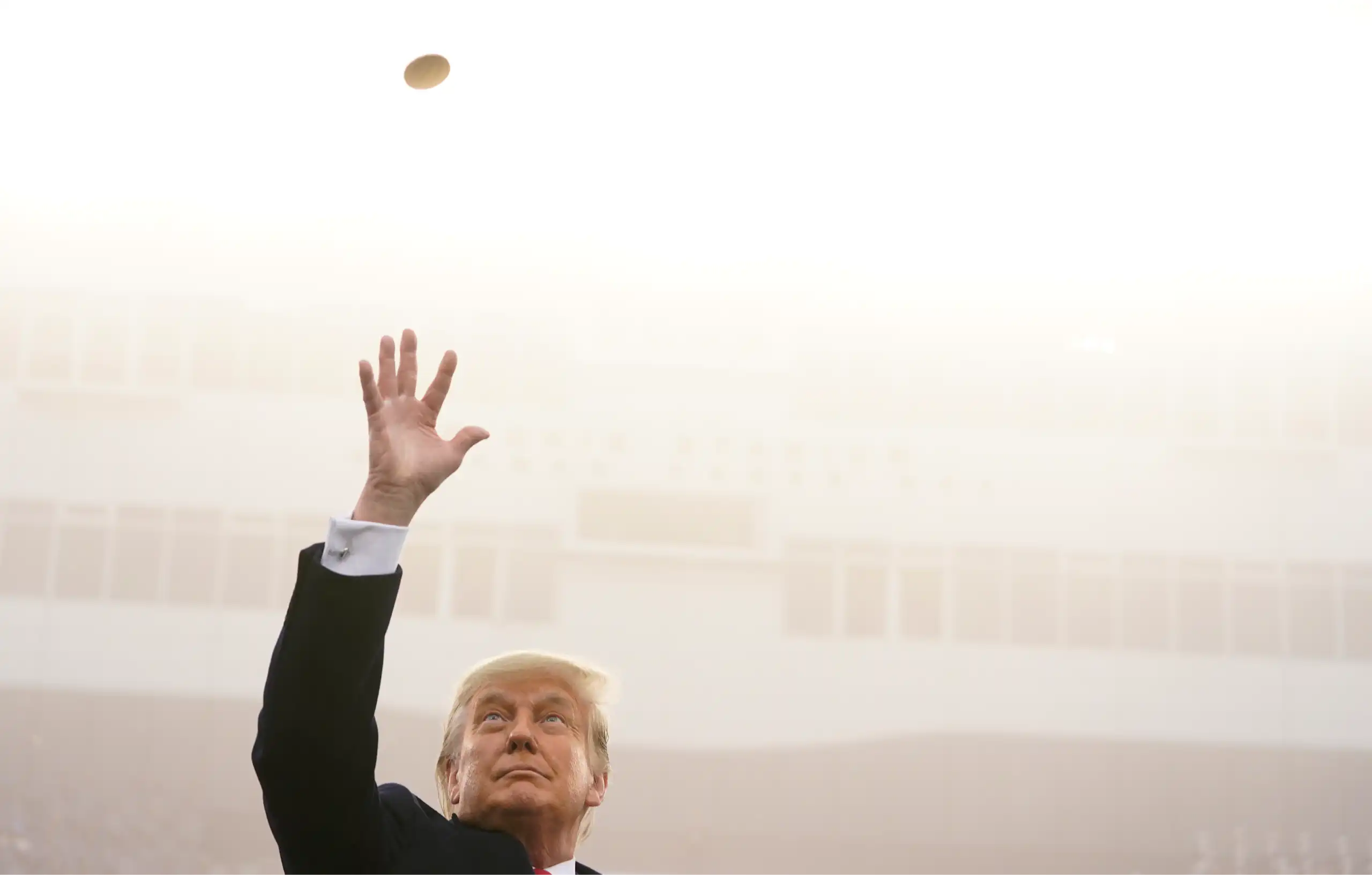 A man in a suit tossing a gold coin in the air.
