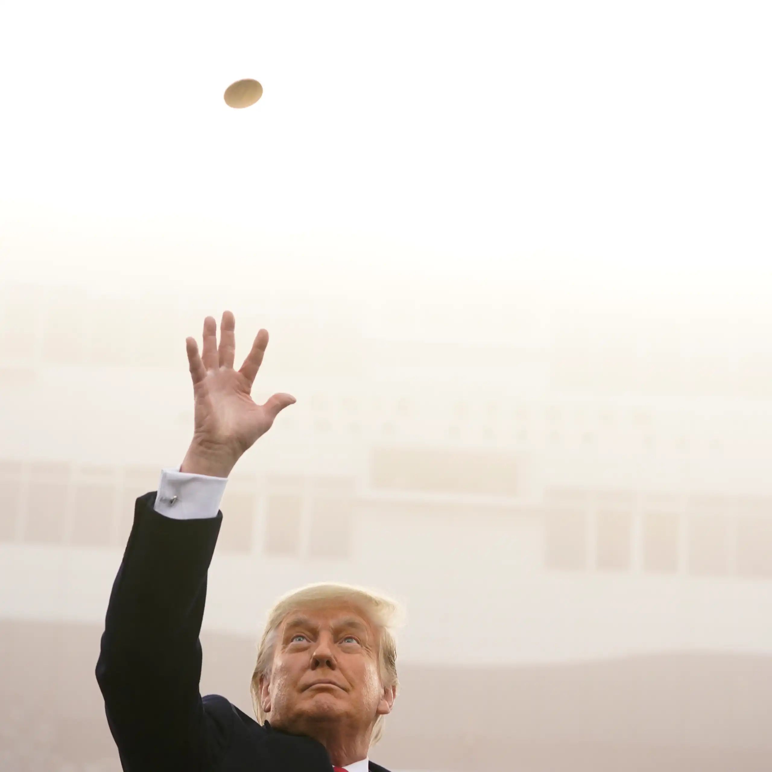 A man in a suit tossing a gold coin in the air.