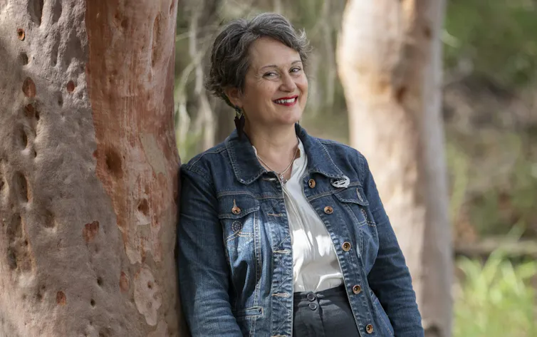 a smiling woman leaning against a gum tree