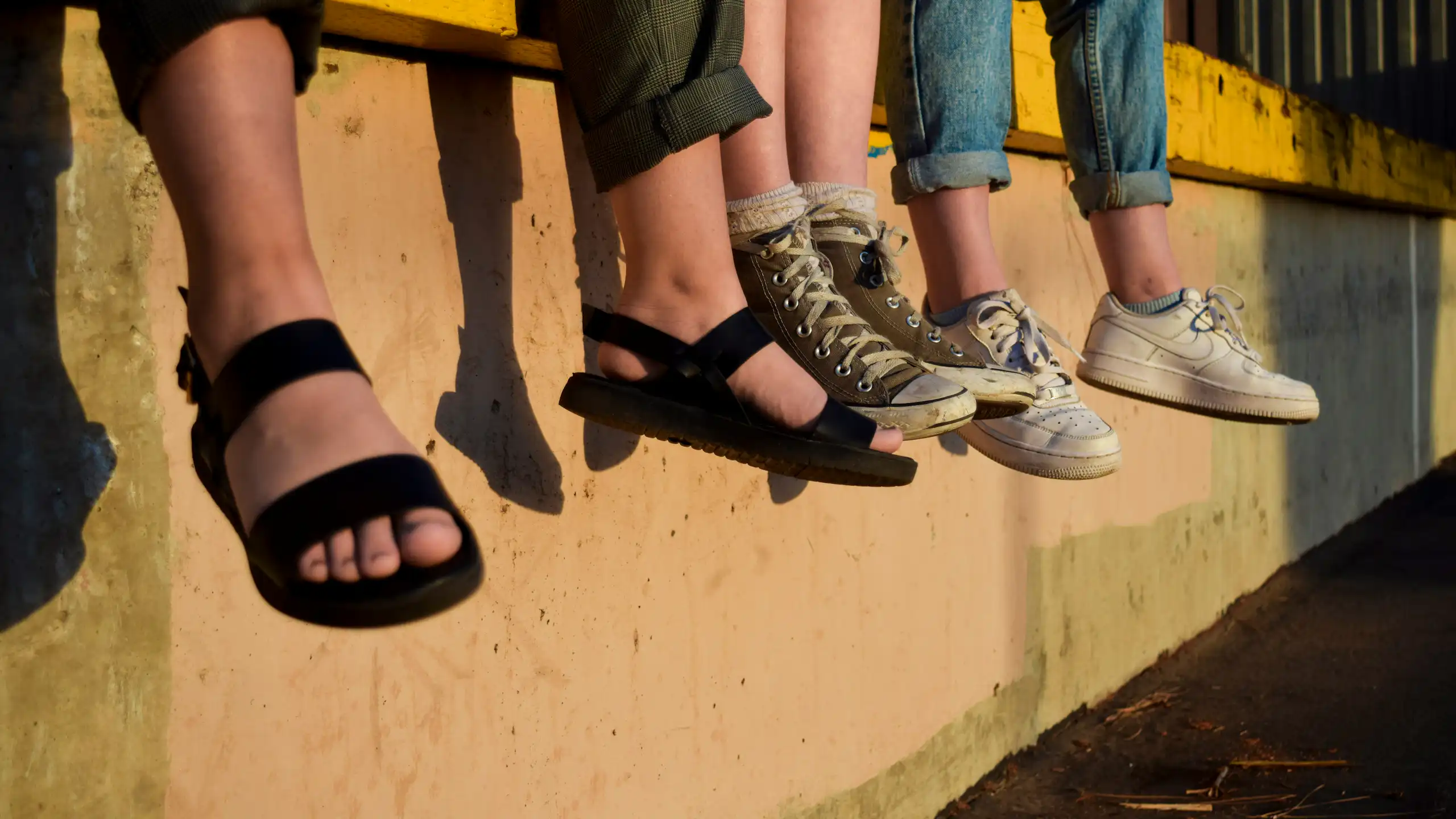 Teens' feet hanging as they sit on a wall.