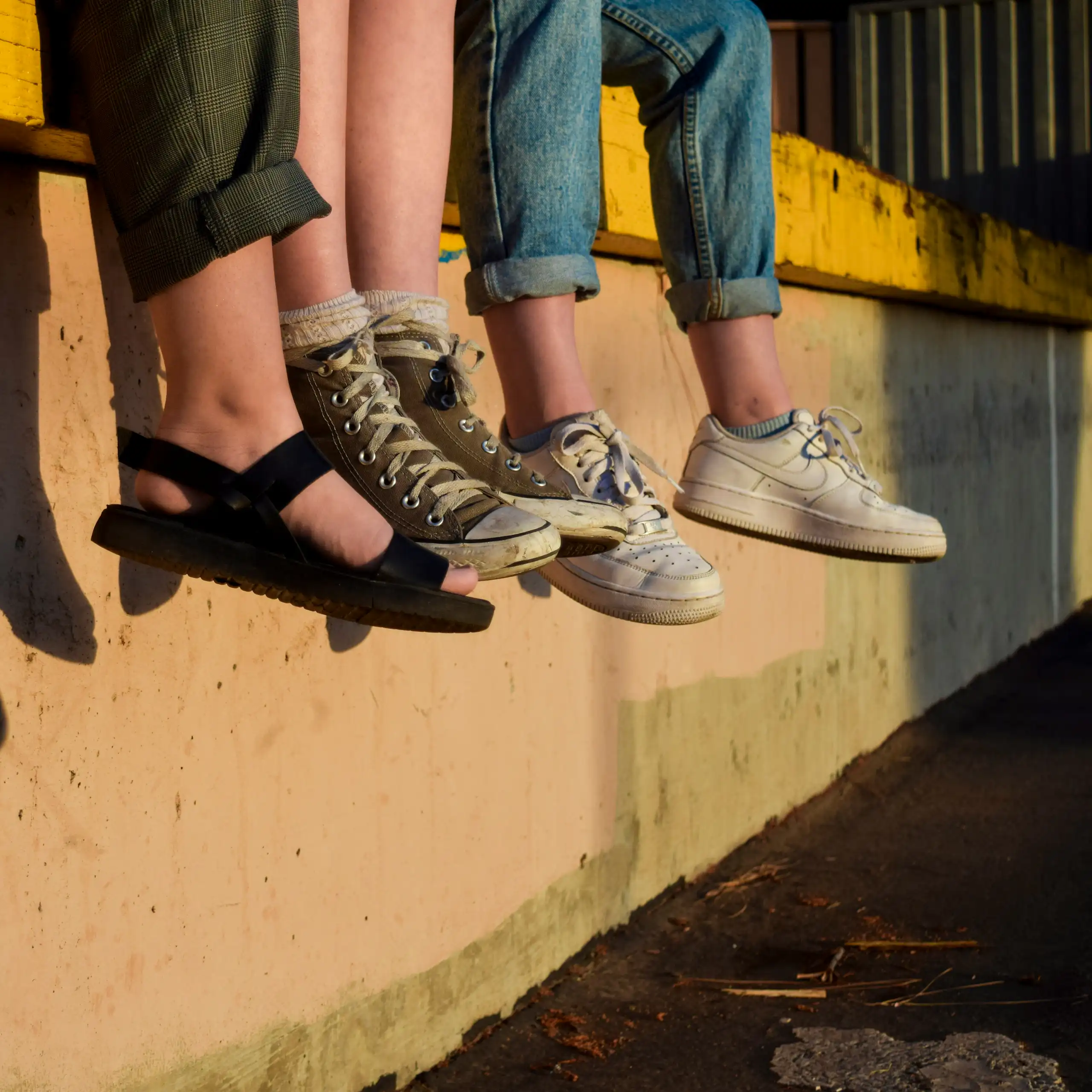 Teens' feet hanging as they sit on a wall.