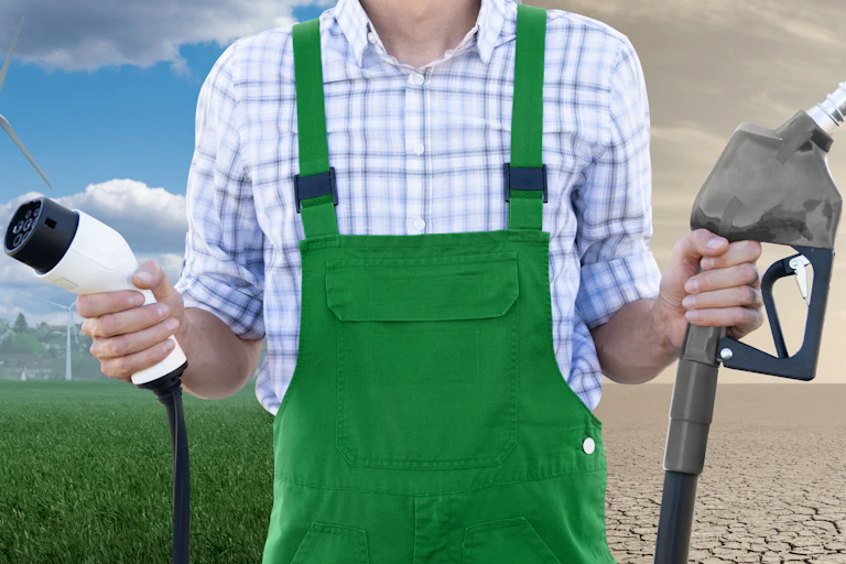 man in green apron and white shirt holds ev charger and fuel nozzle