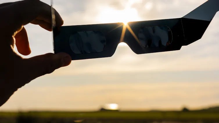 Una mano sujeta unas gafas oscuras en un paisaje rural
