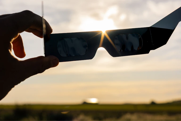 Una mano sujeta unas gafas oscuras en un paisaje rural