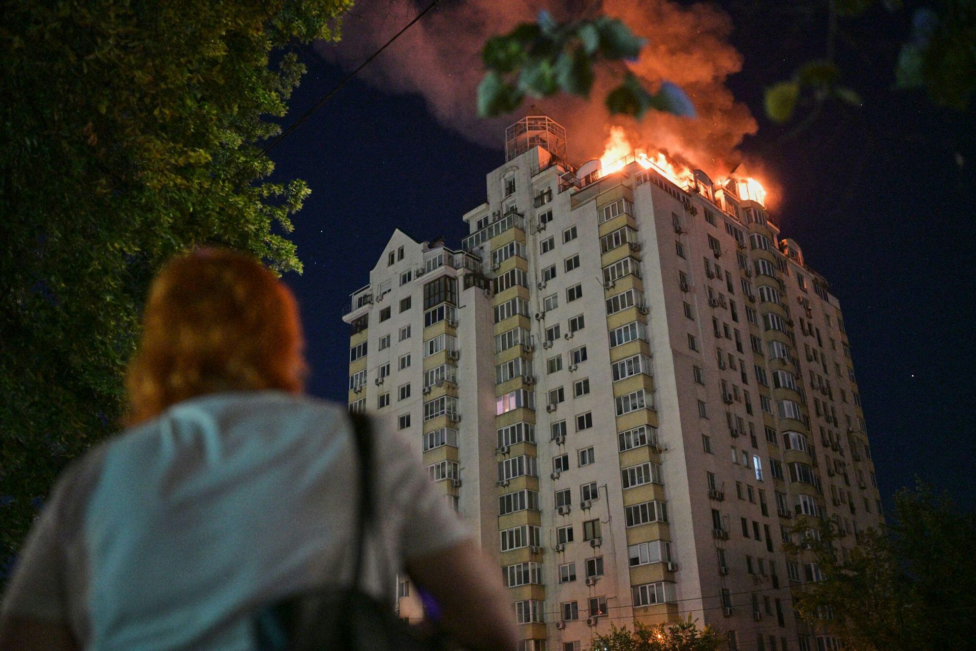 A woman waztches an apartment block burn in Kyiv, July 1 2026.