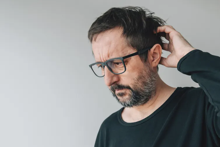 A man scratching his head, seemingly trying to remember something.