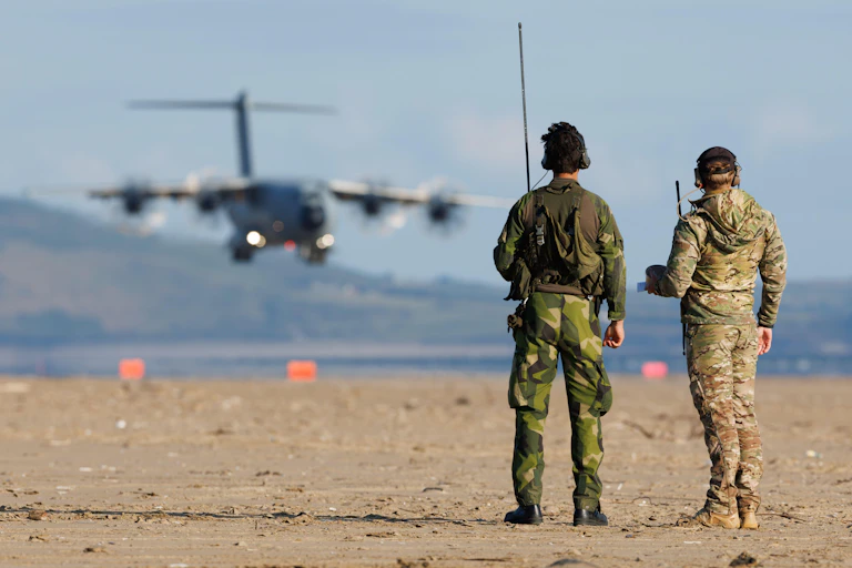 RAF A400 on the beach with two personnel in the foreground.