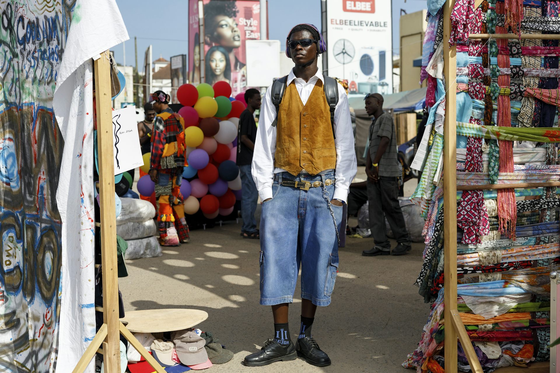 Un jeune Ghanéen vêtu avec style pose devant des présentoirs de tissus récupérés