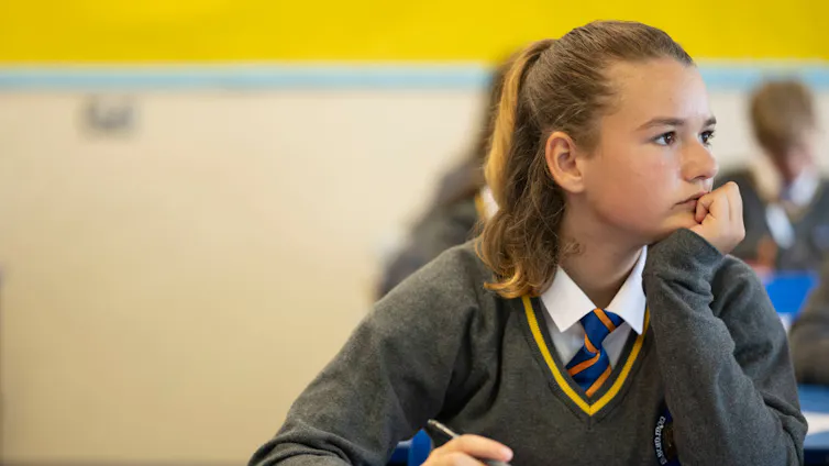 A girl in school uniform looks off to the side in thought.