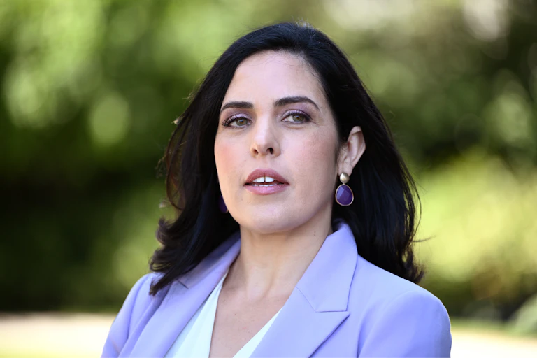 A woman in a purple blazer looks past the camera