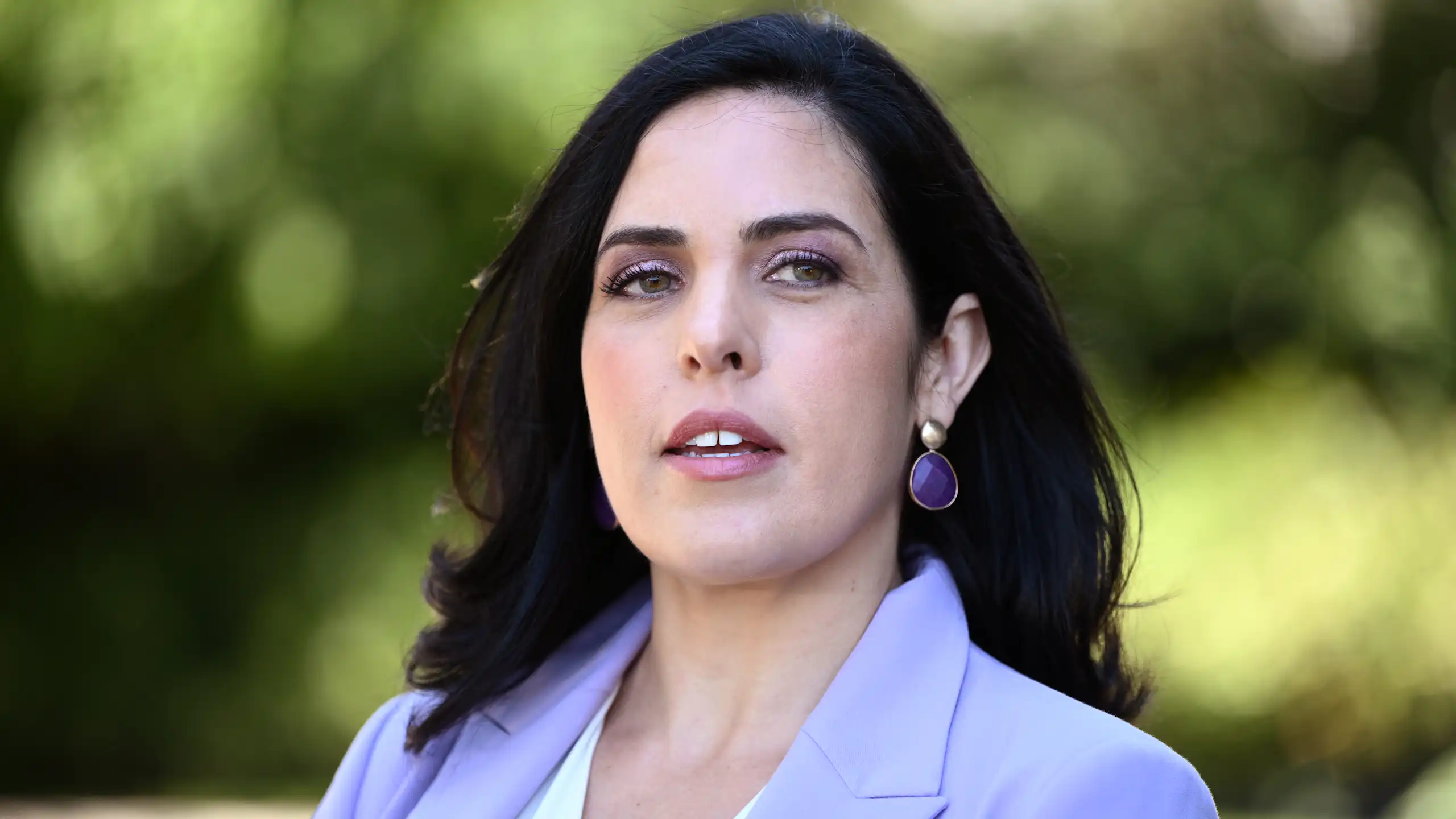 A woman in a purple blazer looks past the camera