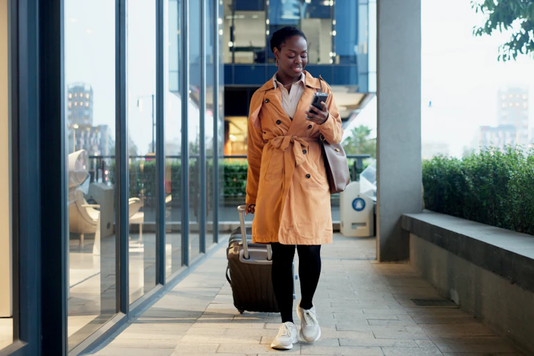 Une femme avance avec sa valise, son téléphone à la main.