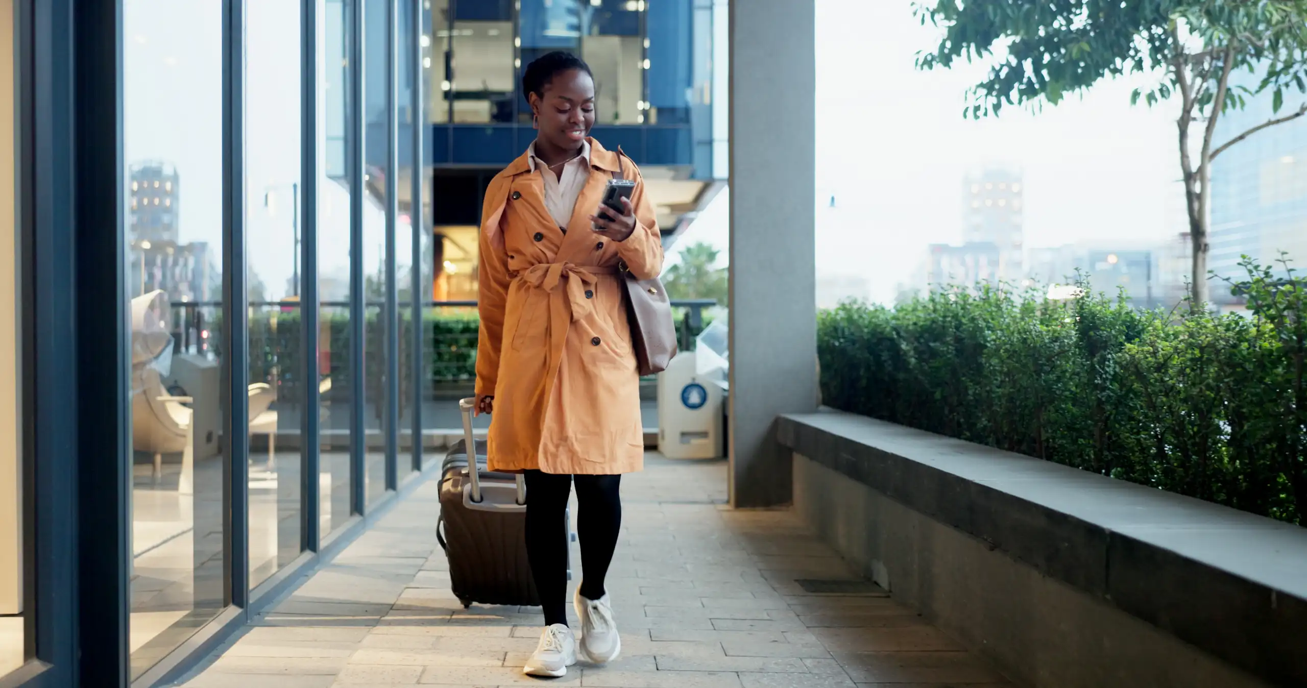 Une femme avance avec sa valise, son téléphone à la main.