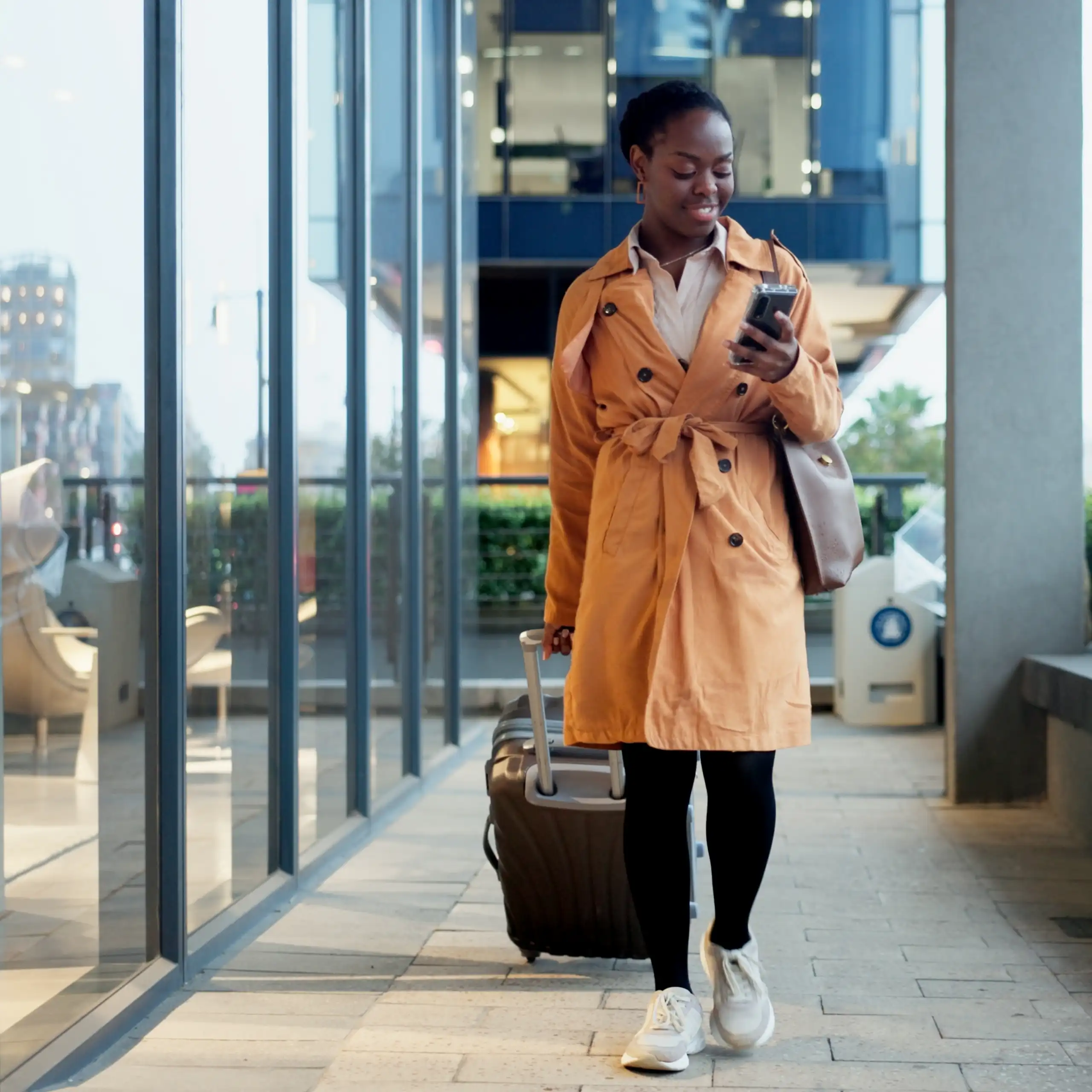 Une femme avance avec sa valise, son téléphone à la main.