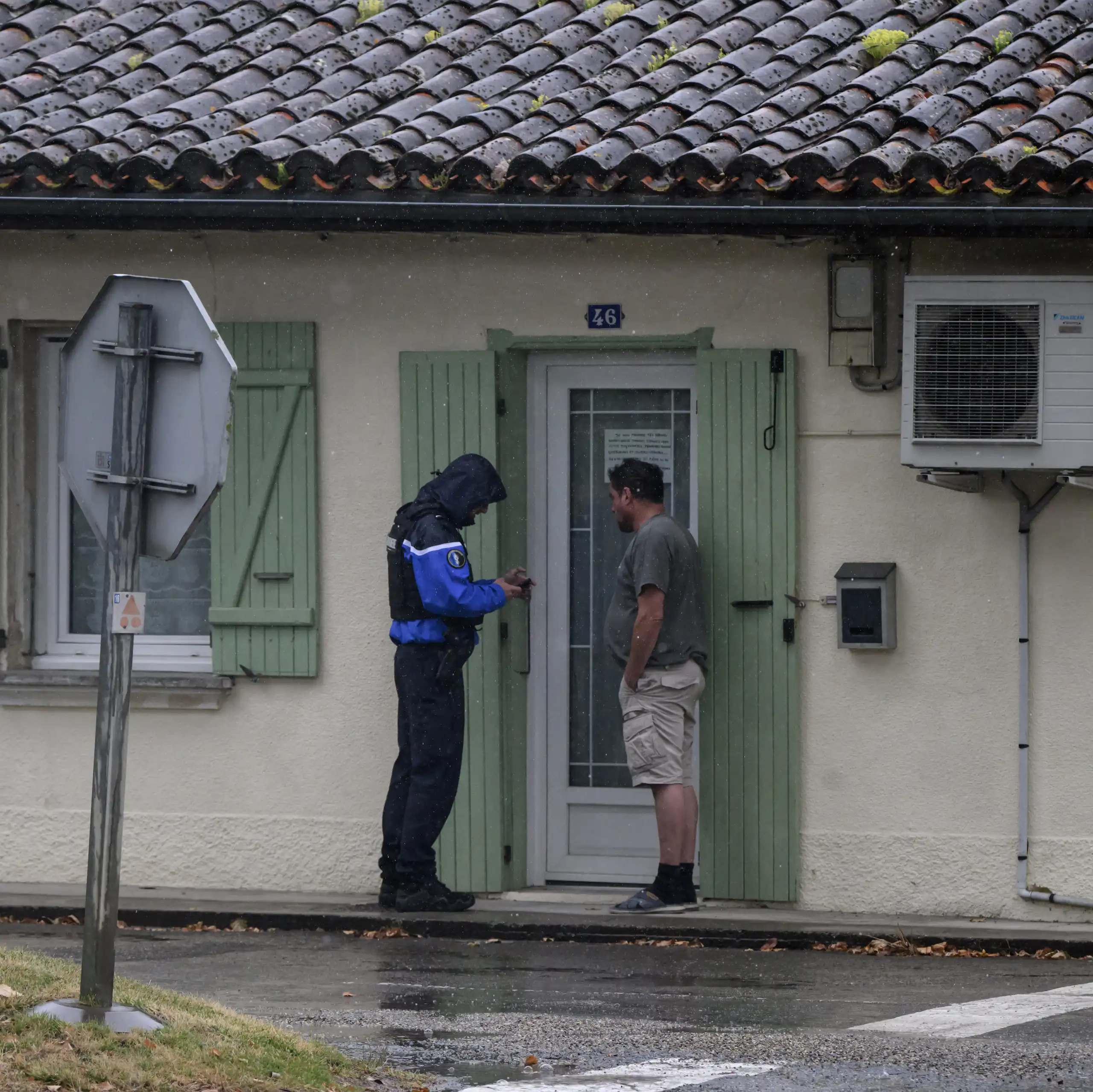 un gendarme parle avec un homme devant la porte de sa maison.