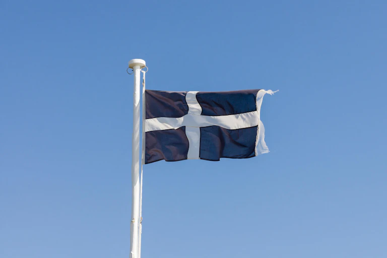 A dark navy flag with a white cross fluttering against a bright blue sky.