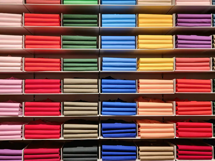 shelves stacked with piles of folded colourful T-shirts, pink, red, green, blue, yellow, purple (from L to R)