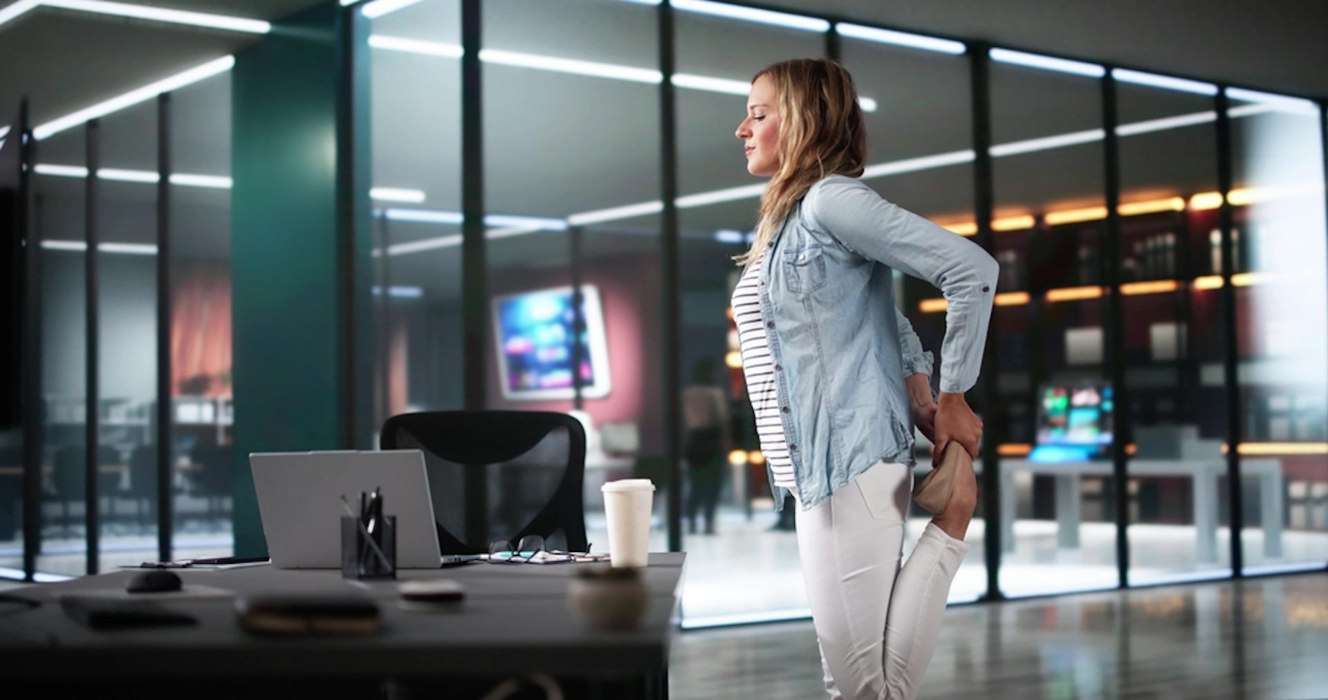 A woman stretching her leg next to her desk.
