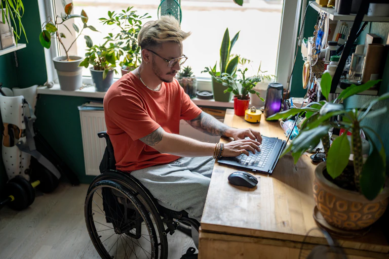 A wheelchair user manages his NDIS plan on his home laptop