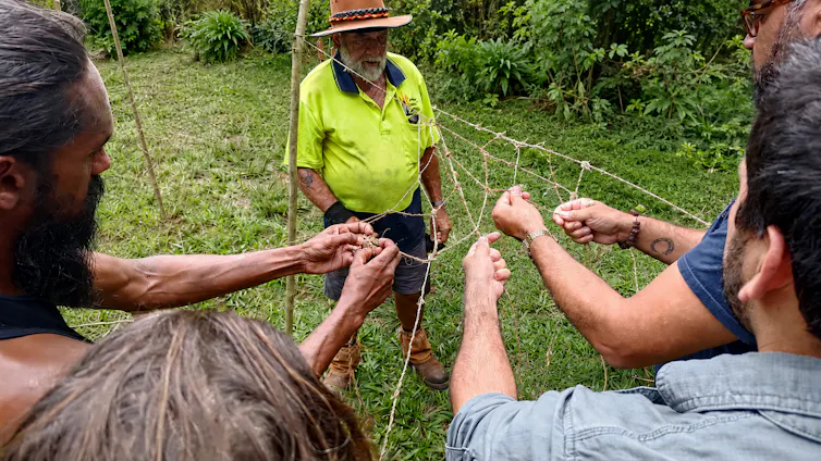 A guide shows a group of men how to make a net.