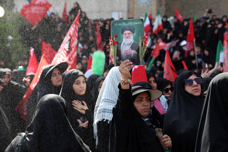 A woman in a crowd of mourners holds up a picture of Ayatollah Ali Khamenei