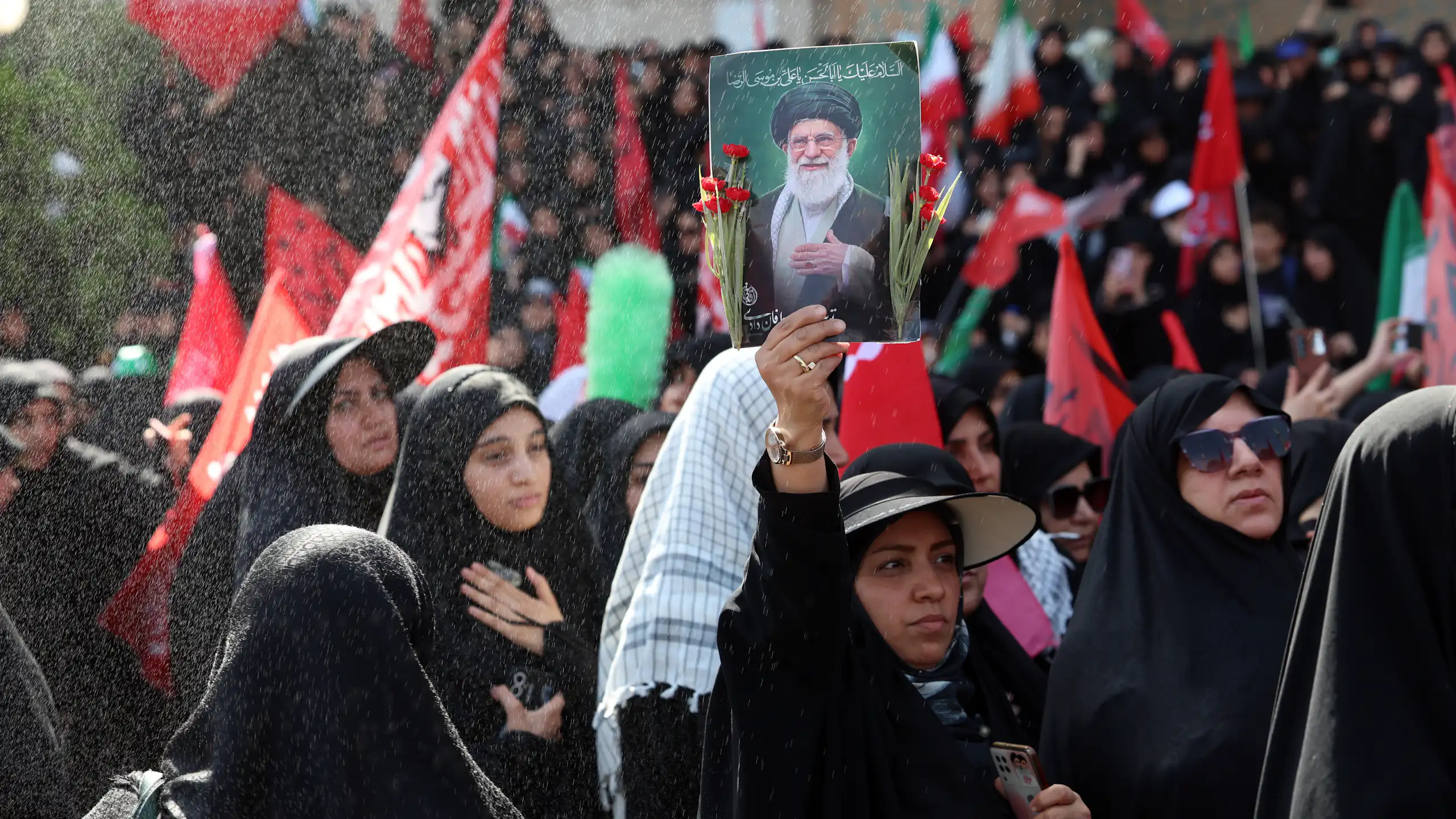 A woman in a crowd of mourners holds up a picture of Ayatollah Ali Khamenei