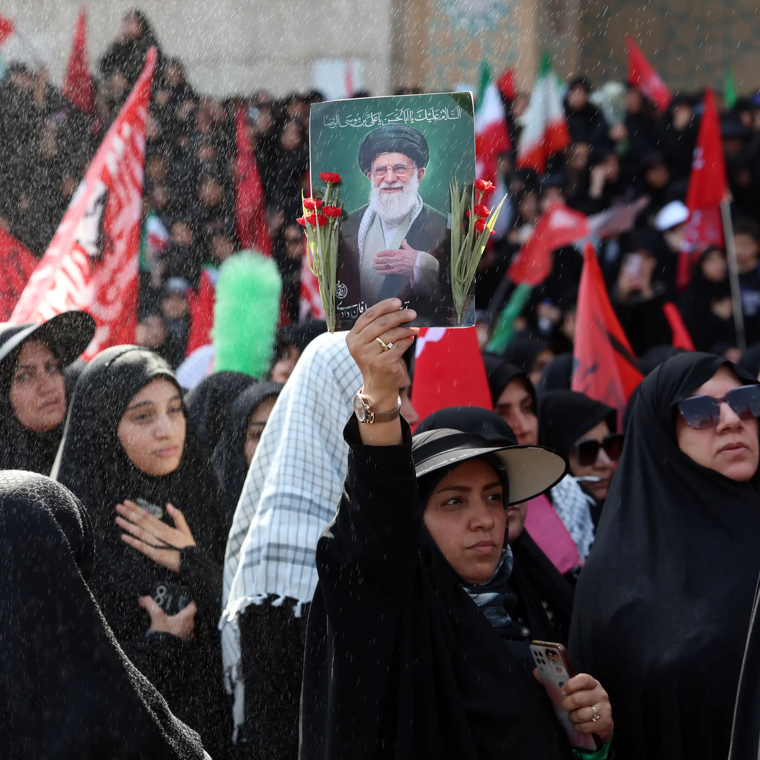 A woman in a crowd of mourners holds up a picture of Ayatollah Ali Khamenei
