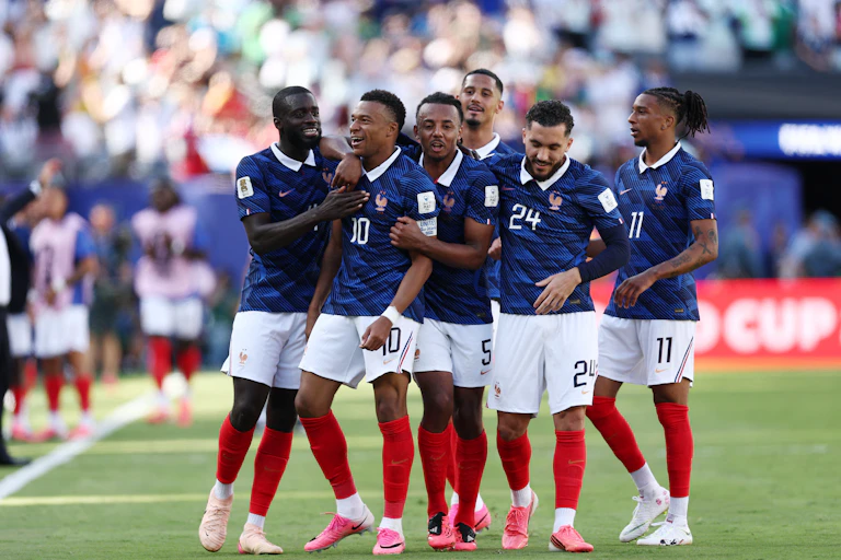 France striker Kylian Mbappé is congratulated by his teammates on the football field.