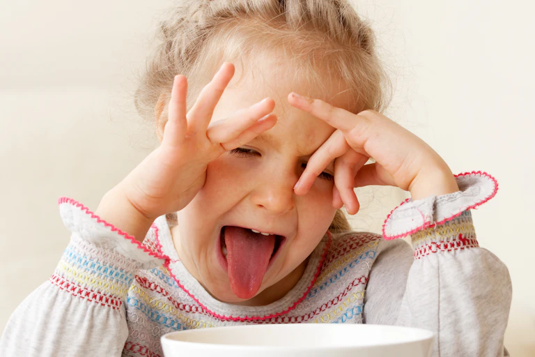 A girl makes a disgusted face when presented with a bowl of food.