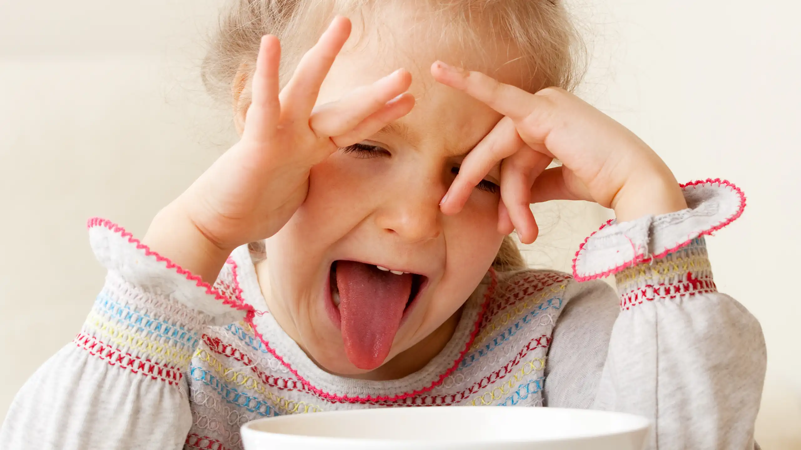 A girl makes a disgusted face when presented with a bowl of food.