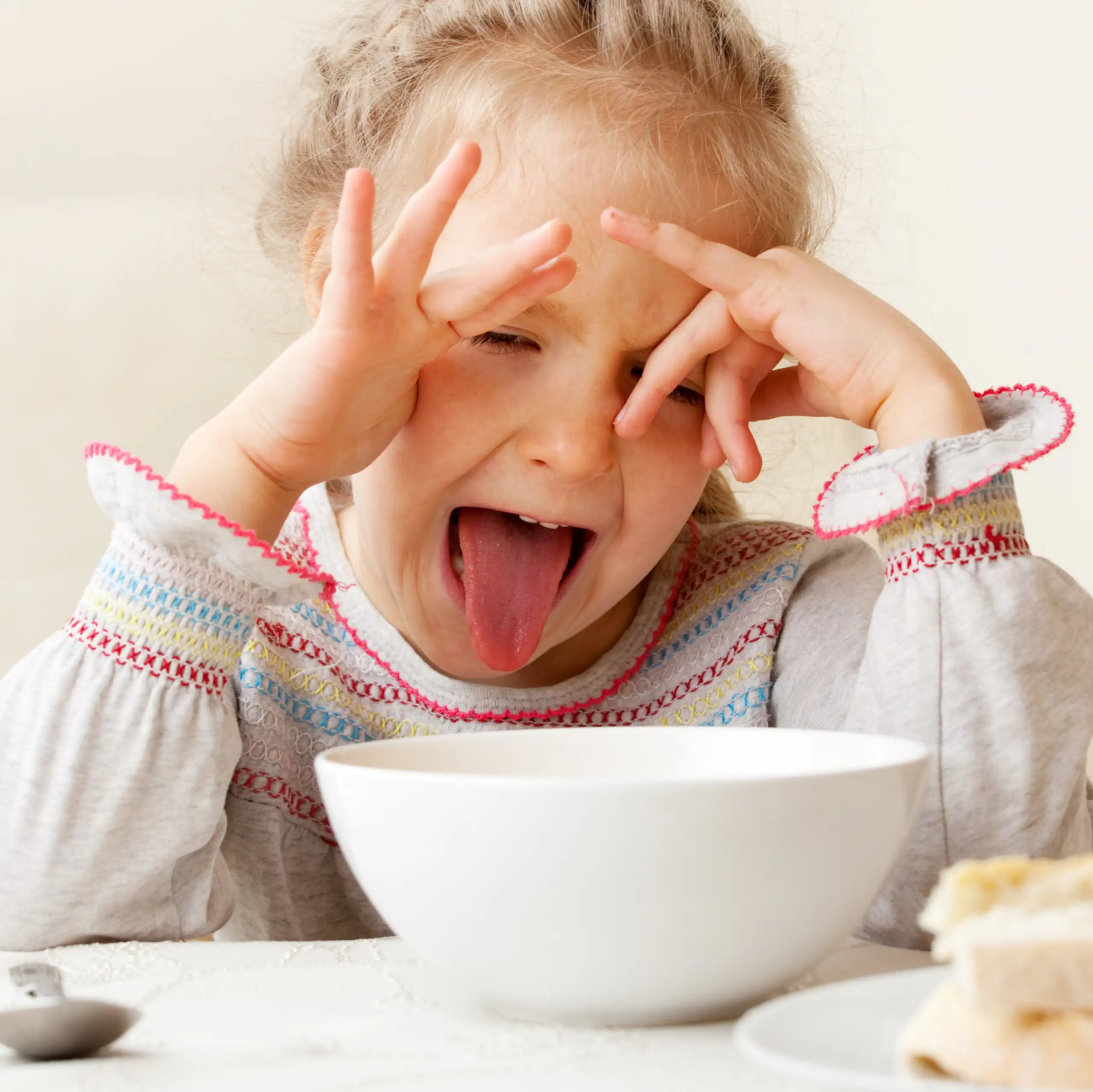 A girl makes a disgusted face when presented with a bowl of food.