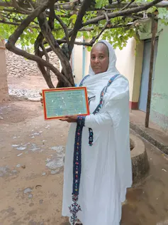 woman standing under a vine, holding a framed certificate