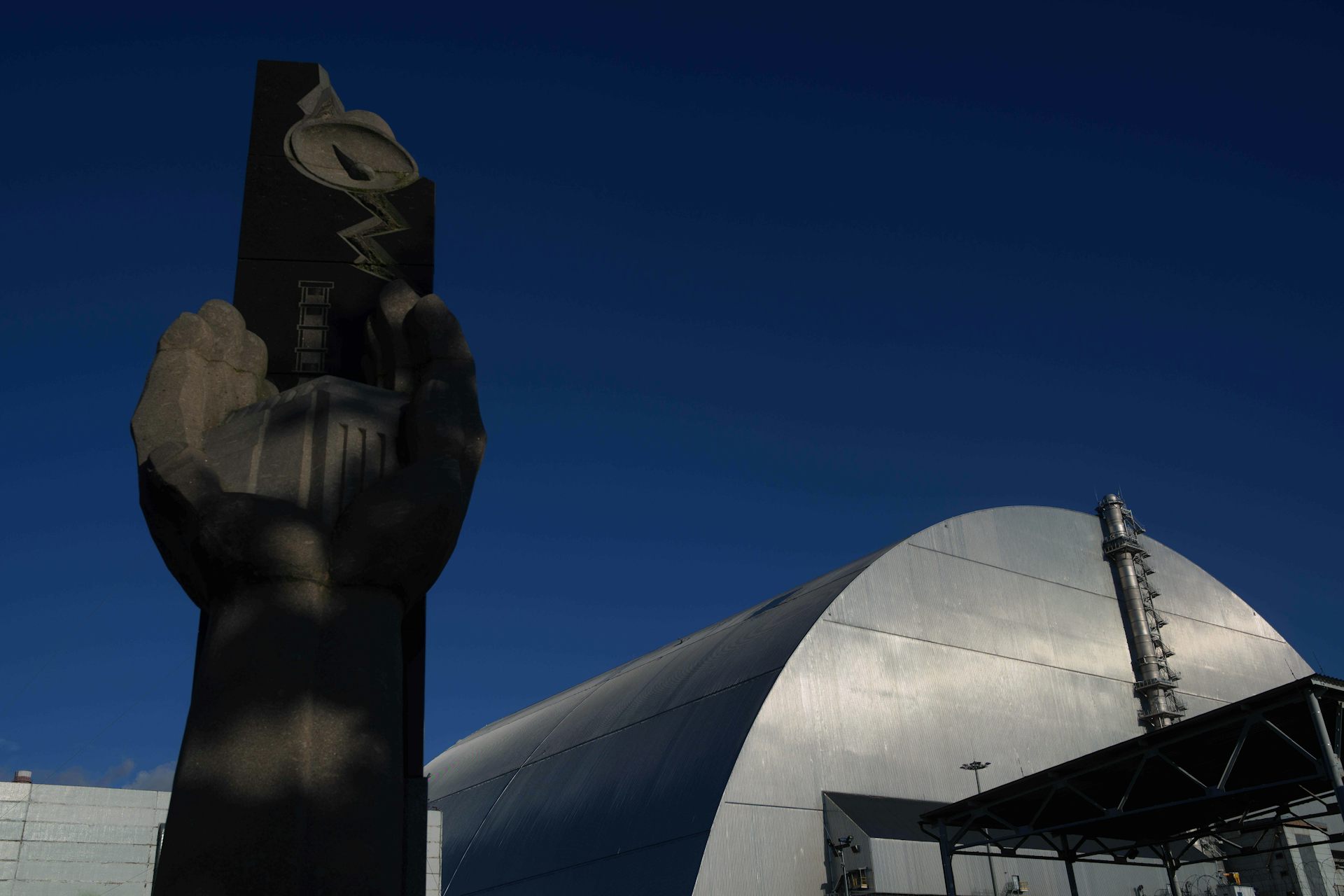 Una estatua de piedra junto a una gran estructura arqueada de metal.