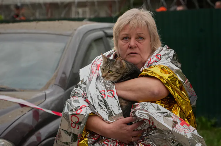 Los ataques con drones en Ucrania tienen impacto en Rusia, pero los líderes rusos siguen comprometidos con la guerra 1 Una mujer rubia con lágrimas en los ojos carga un gato desde un edificio de apartamentos en ruinas.