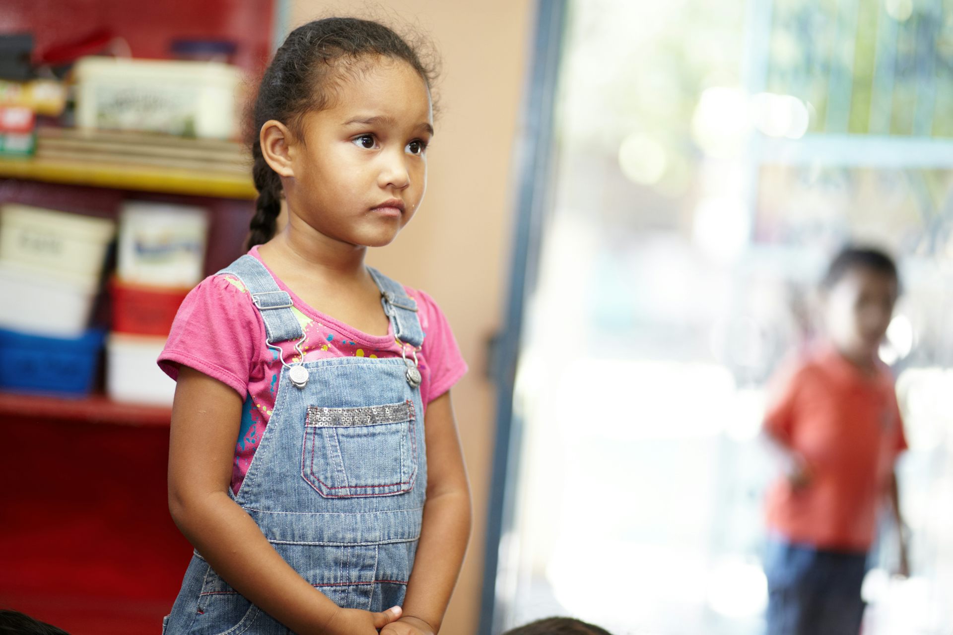 Photo d’une petite fille debout dans une salle de classe l’air vaguement inquiète
