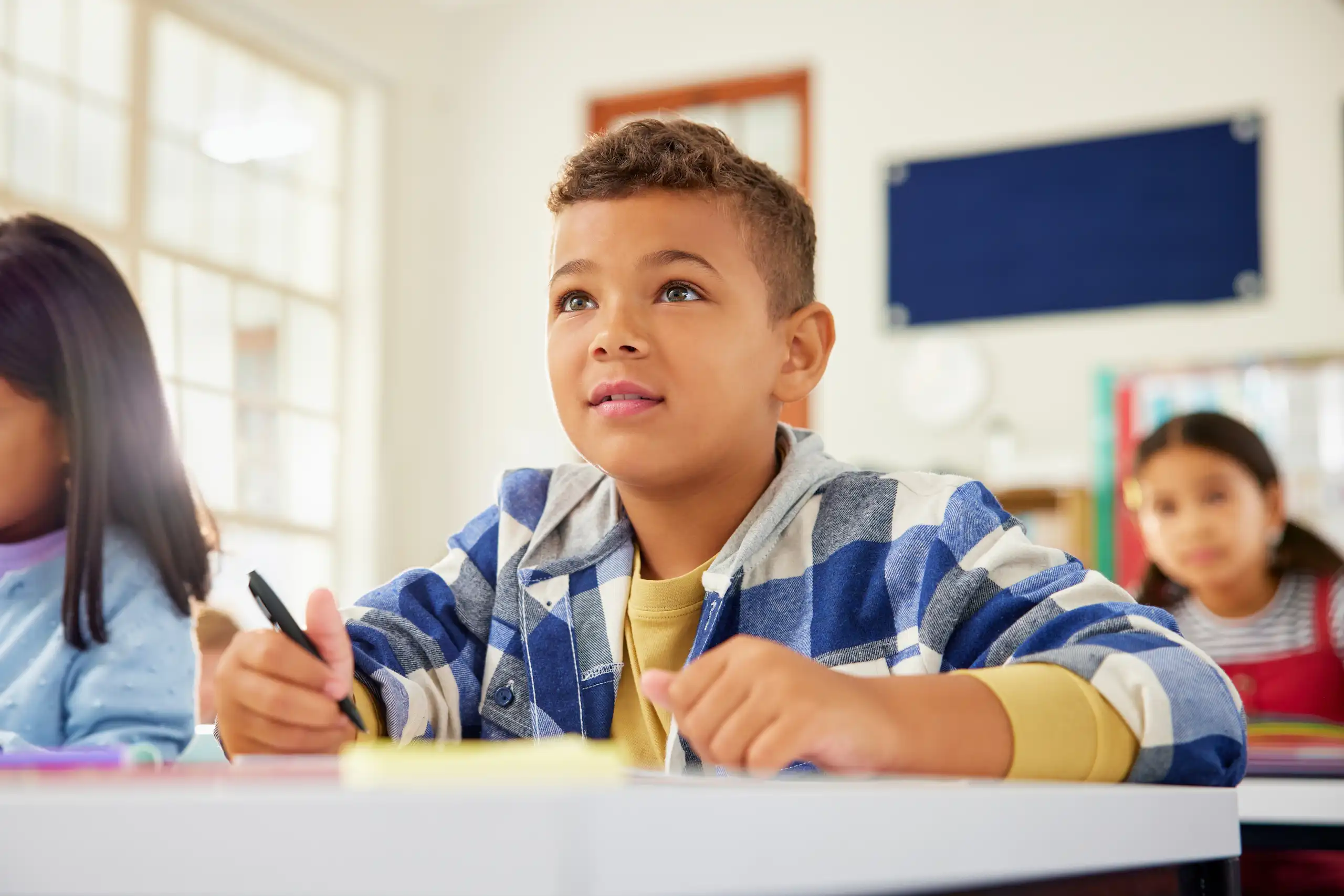 Un jeune garçon est assis à son pupitre d’écolier, visiblement concentré.