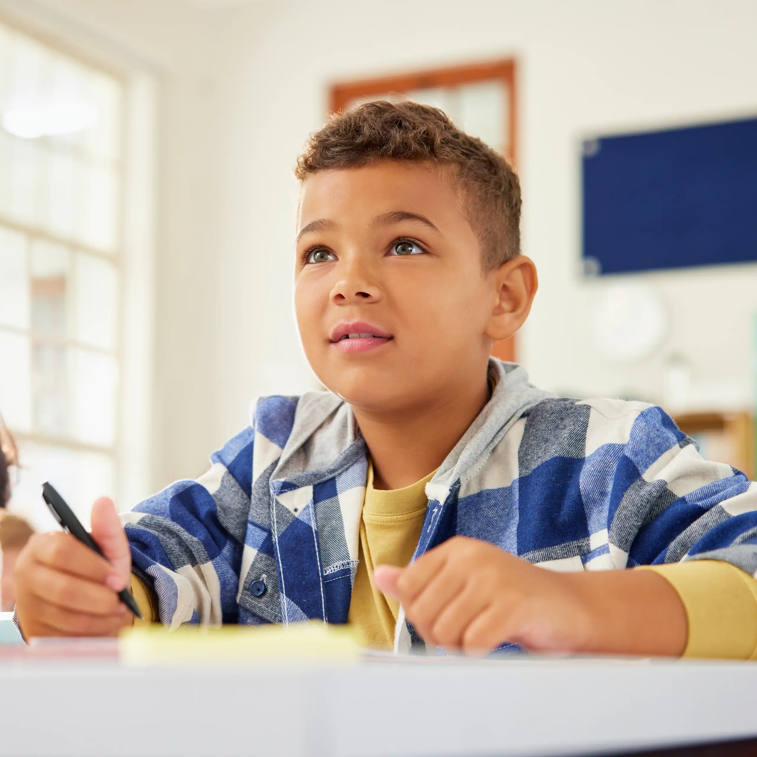 Un jeune garçon est assis à son pupitre d’écolier, visiblement concentré.