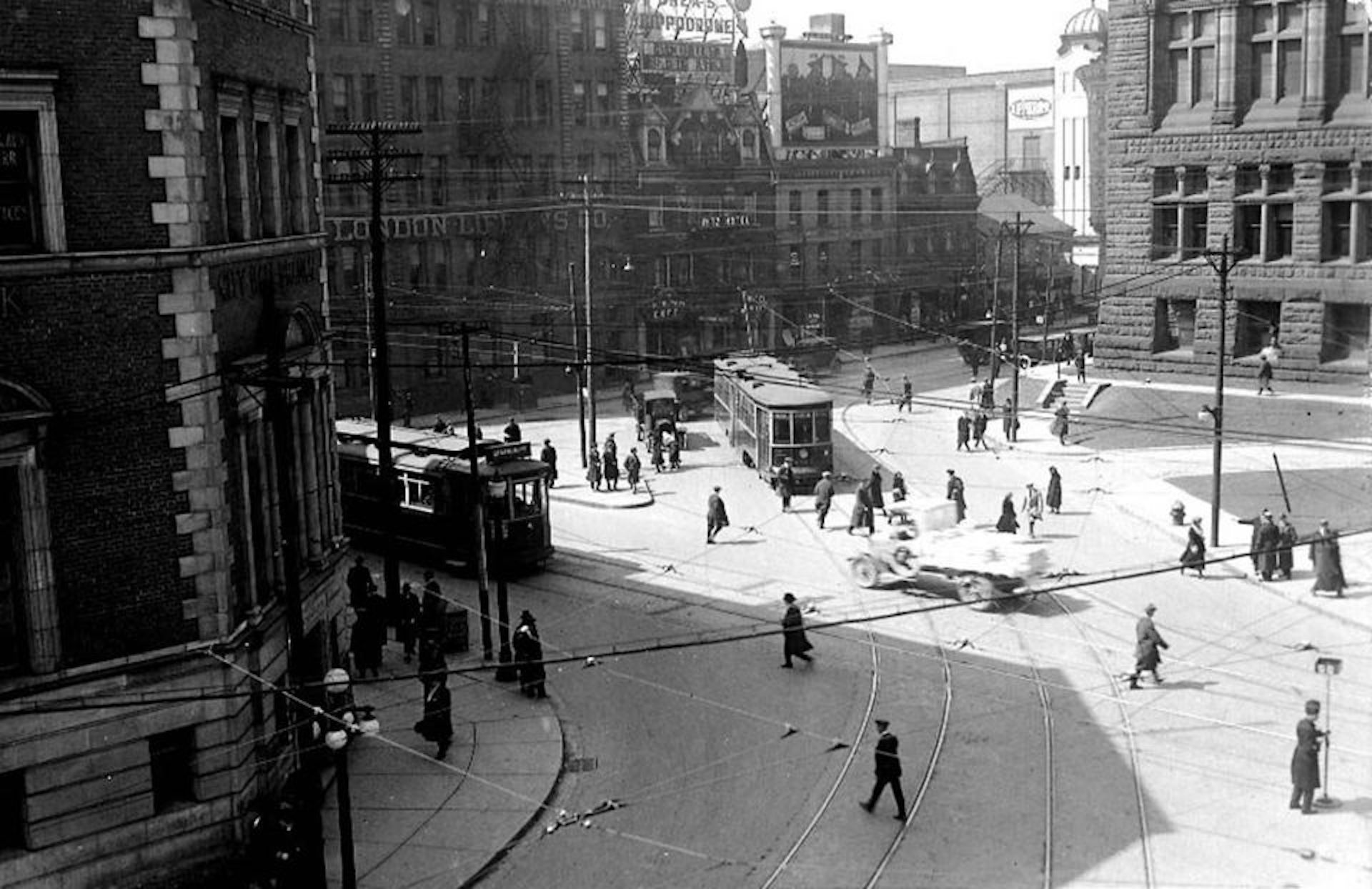 Black and white photo of city streets with a streetcar coming into view and 1920s style cars on the road.