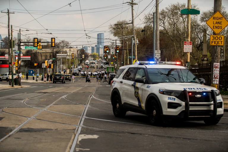 Police car with flashing lights drives through urban area with skyscrapers in background