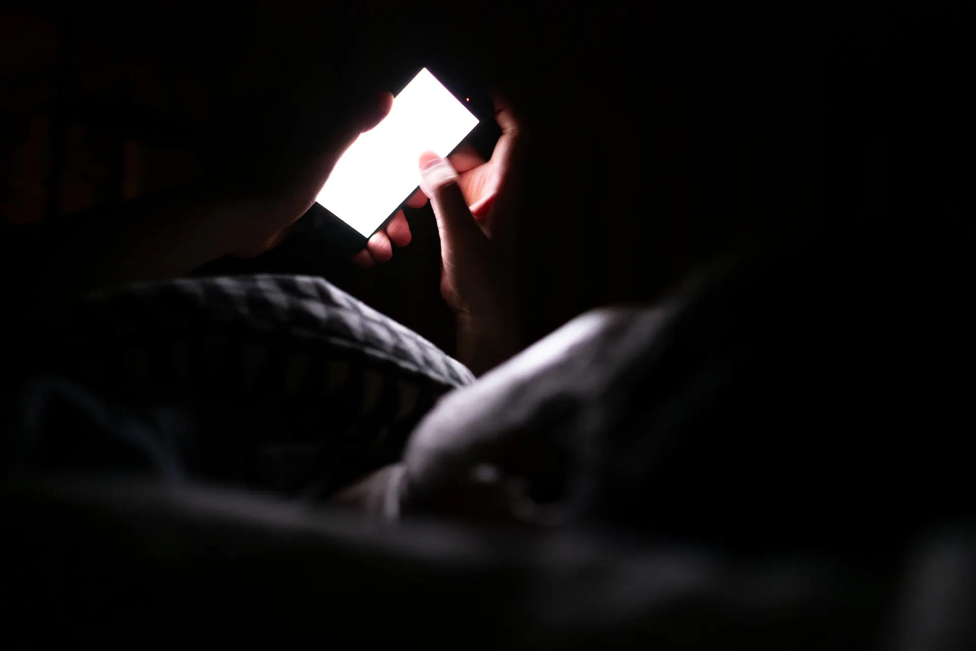Person laying in bed looking at white glow of phone screen