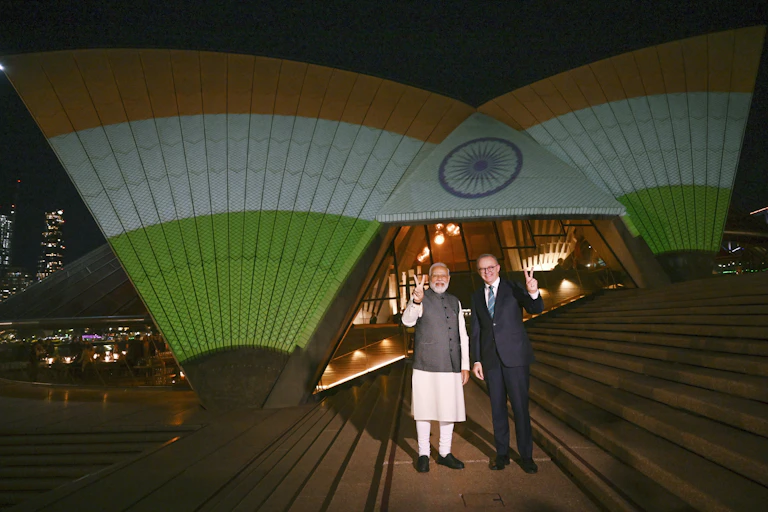 Two men stand in front of the Sydney Opera House lit up in the Indian flag