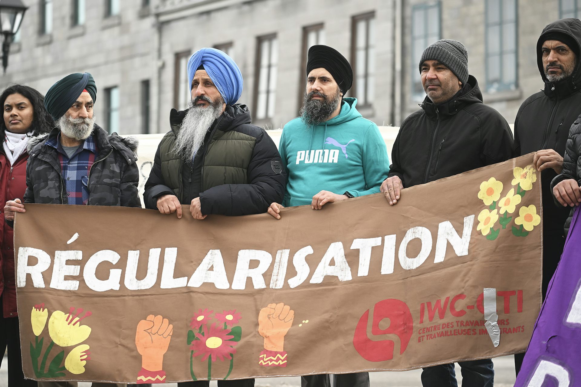 Cinco hombres sostienen una gran pancarta marrón con ilustraciones y la palabra regularización.