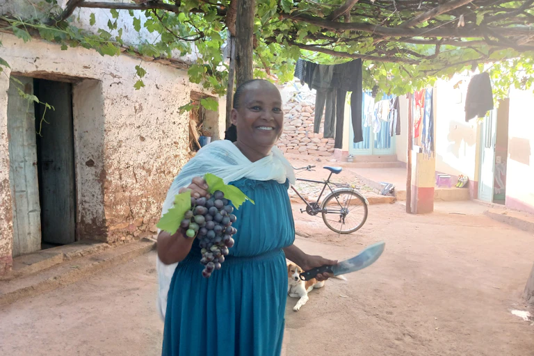 Woman holding grapes while standing under a vine on a trellis