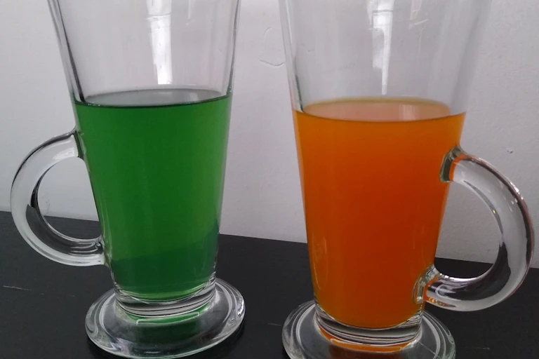 Two glasses, one containing a green liquid and the other an orange liquid