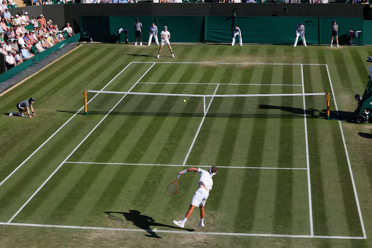 Whole-court view of a player serving at Wimbledon as his opponent prepares to return the serve.